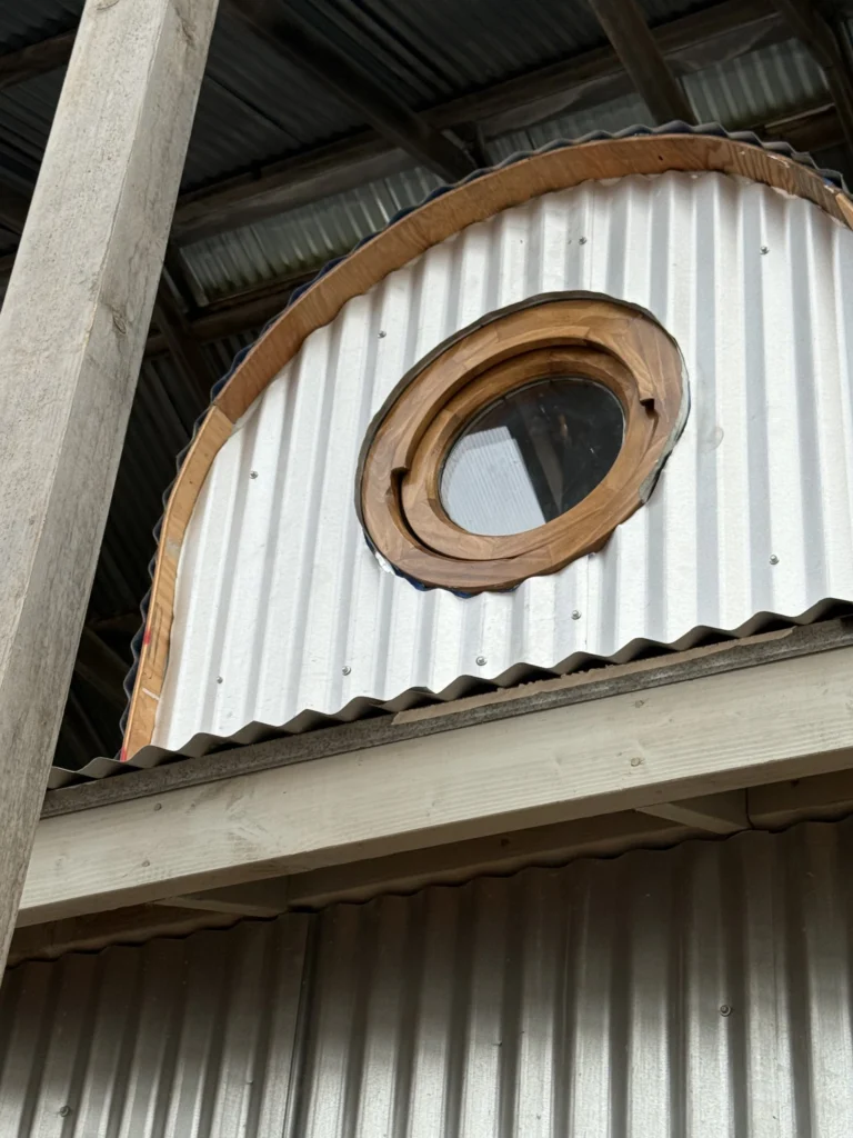 Whole-house remodel: Round window set into an arched corrugated metal wall, Bolinas