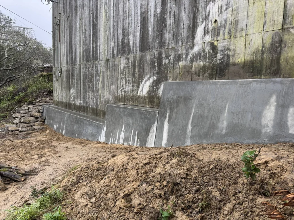 Hardscape: New concrete retaining wall along the base of an old barn, Bolinas