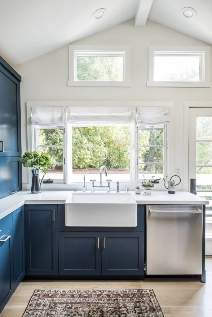 Kitchen remodel: Farmhouse sink under casement windows and transoms, navy cabinets and stainless dishwasher