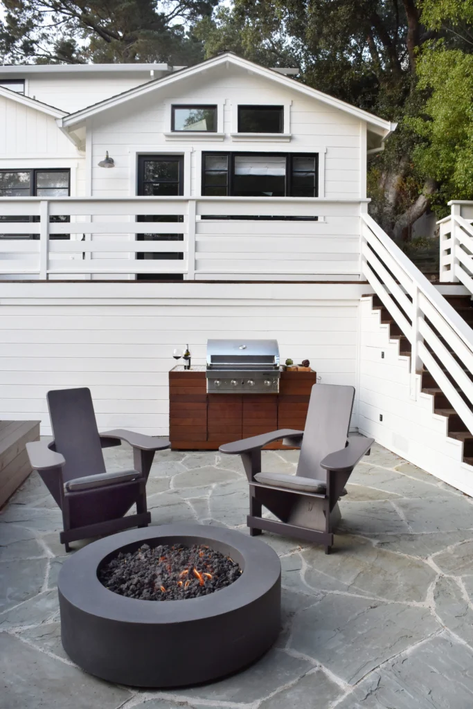 Deck: Flagstone patio with fire pit and built-in grill below white house with deck railing and stairs