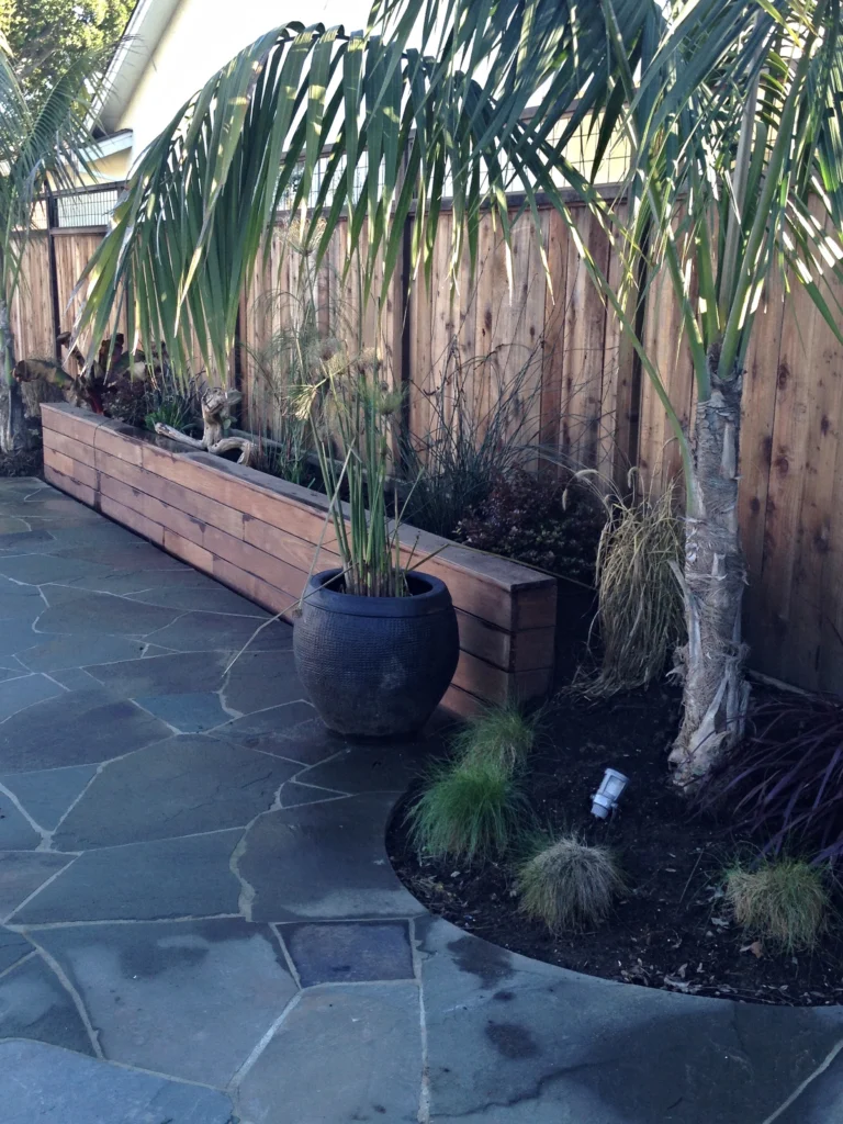 Fencing: Flagstone patio beside a long wood planter box and redwood fence, with palms and a dark glazed pot