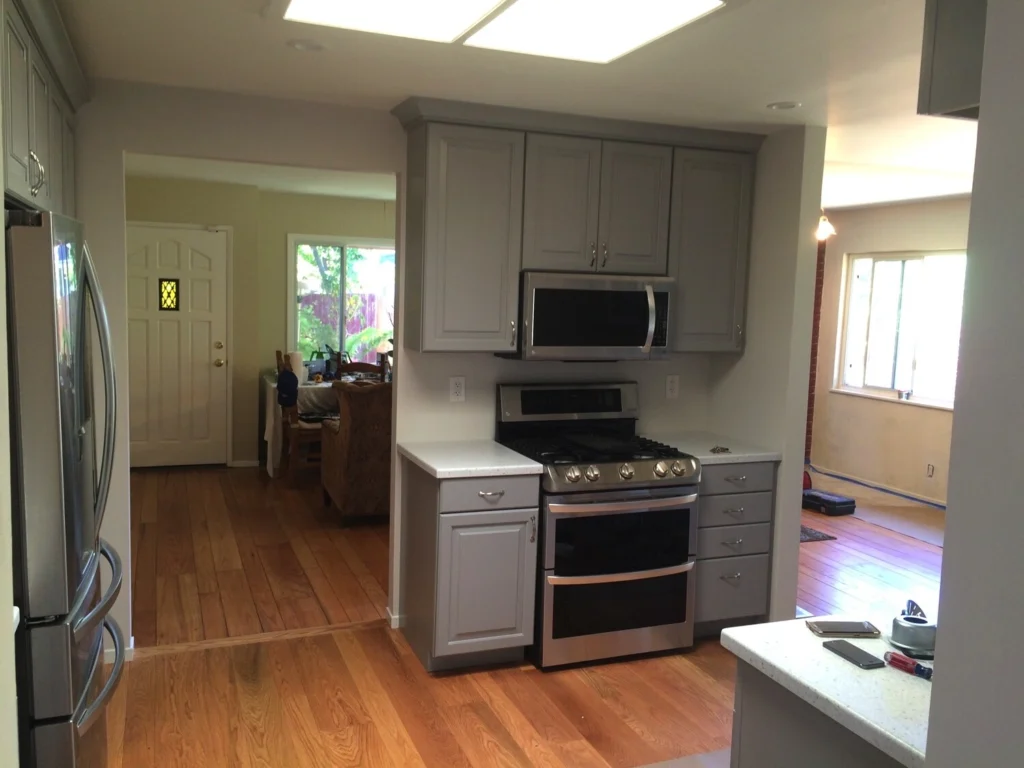 Flooring: Grey raised-panel cabinets with stainless gas range and microwave over oak hardwood floor