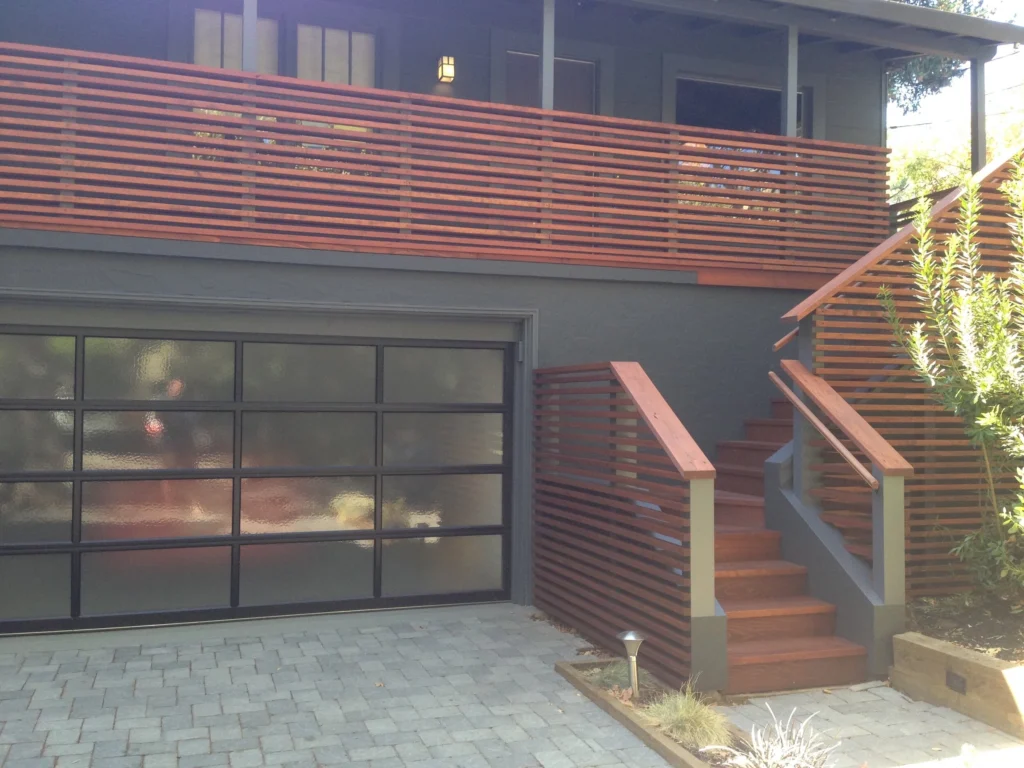 Deck: Horizontal slat redwood railings and stairs on a grey house, with frosted glass garage door and paver driveway