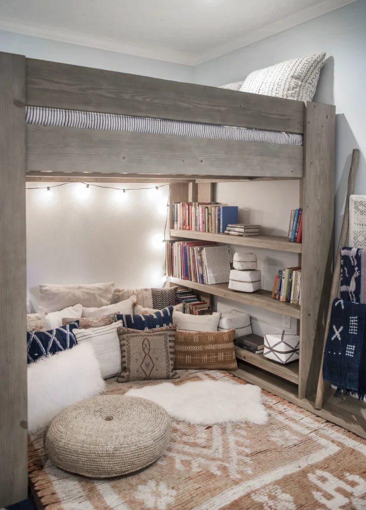 Whole-house remodel: Grey wood loft bed over a reading nook with built-in bookshelves, cushions and string lights