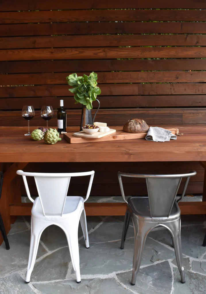 Deck: Wood outdoor dining table and metal chairs in front of horizontal slat screen on flagstone