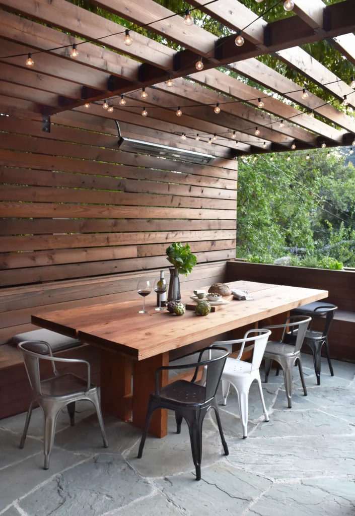 Deck: Outdoor dining area under wood pergola with string lights, heater, slat wall and flagstone