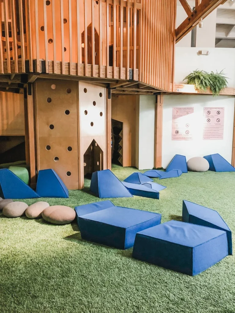 Treehouse tower and soft blue play blocks on a turf floor in a children's play space