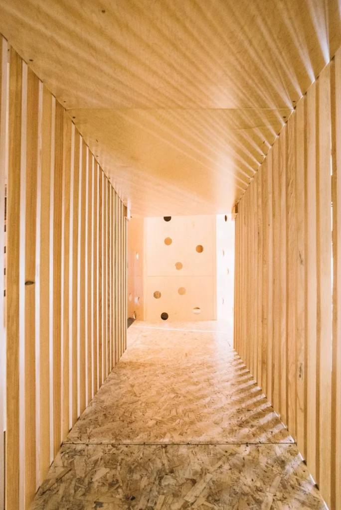 Wood slat tunnel leading to a climbing wall in a children's play space
