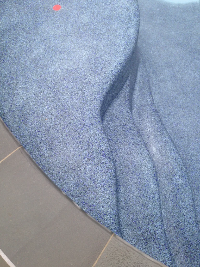 Hardscape: Close-up of blue pebble pool finish on curved steps next to grey stone coping