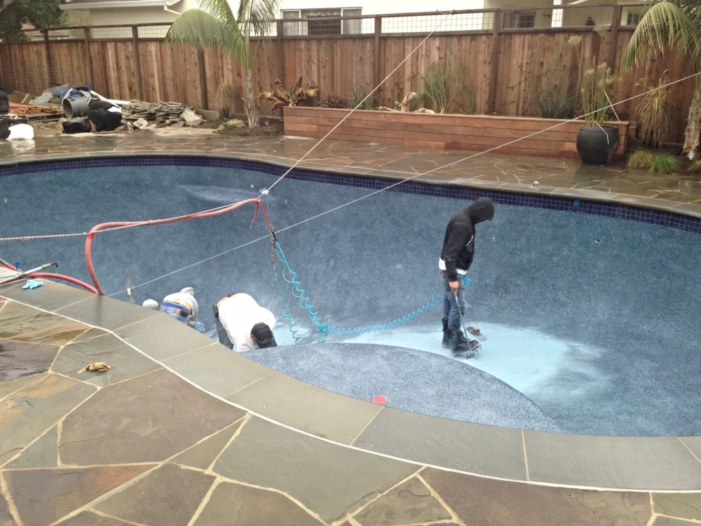 Hardscape: Crew working inside a drained pool with new flagstone deck, wood planter box and redwood fence around it