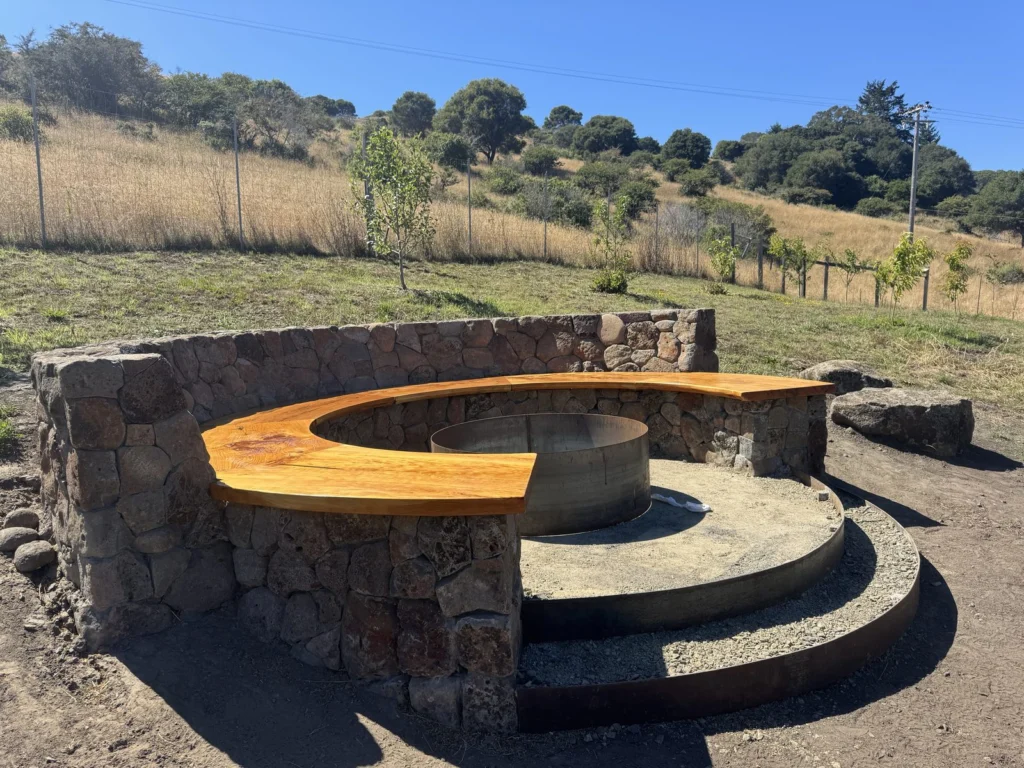 Hardscape: Stone fire pit seating wall with a curved wood bench, below the hills, Bolinas