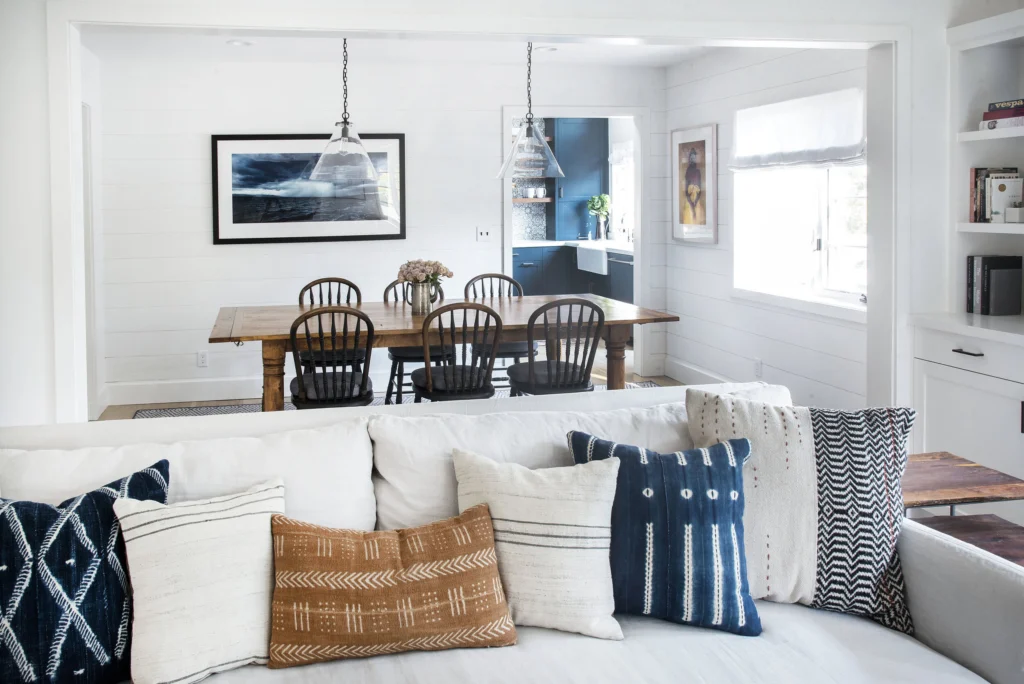 Whole-house remodel: View past sofa into shiplap dining room with glass pendants and the navy kitchen beyond