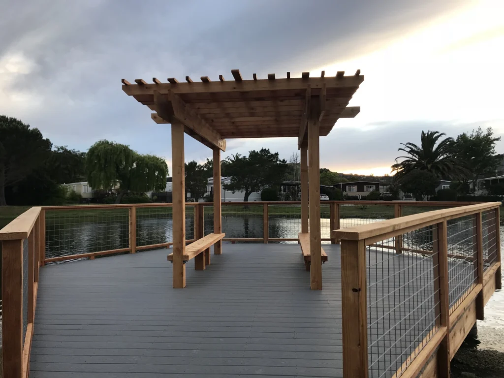 Deck: Grey composite deck with a cedar pergola, built-in benches and wood rail with wire mesh panels by the water
