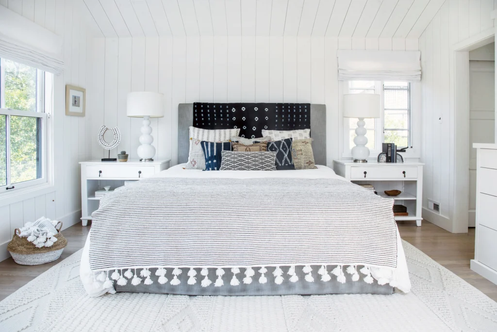 Whole-house remodel: Bedroom with white vertical board walls and ceiling, casement windows and Roman shades