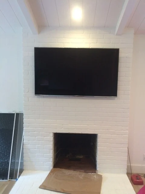 Whole-house remodel: Painted white brick fireplace with wall-mounted TV and plank ceiling, hearth still covered