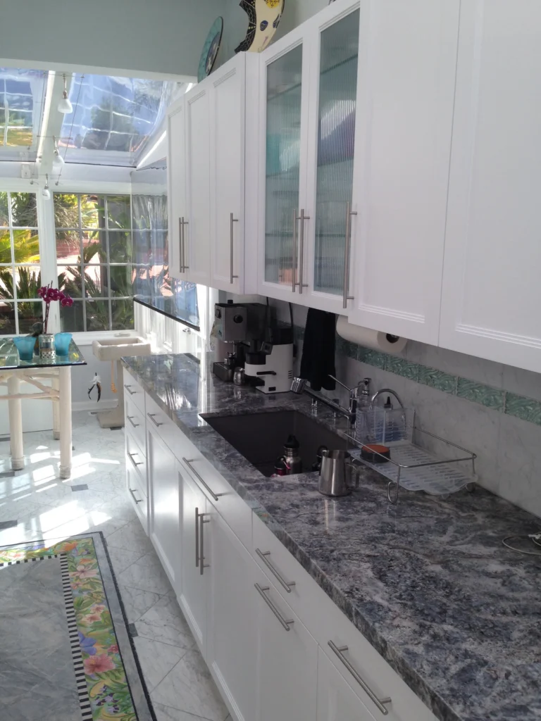 Flooring: White shaker kitchen with blue-grey granite, undermount sink and marble floor, opening to a glass sunroom
