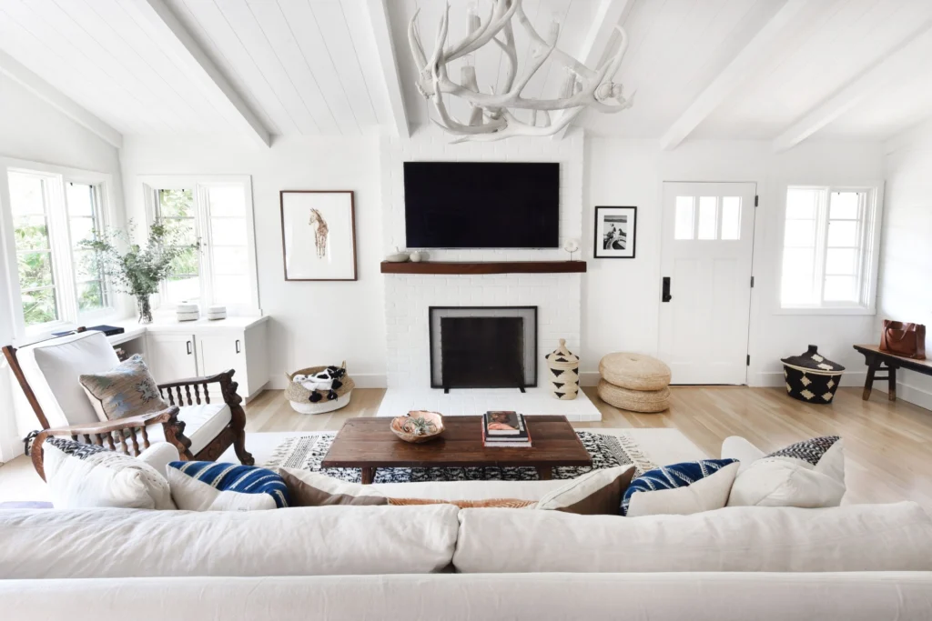 Flooring: Bright living room with painted white brick fireplace, wood mantel, beamed plank ceiling and light oak floors