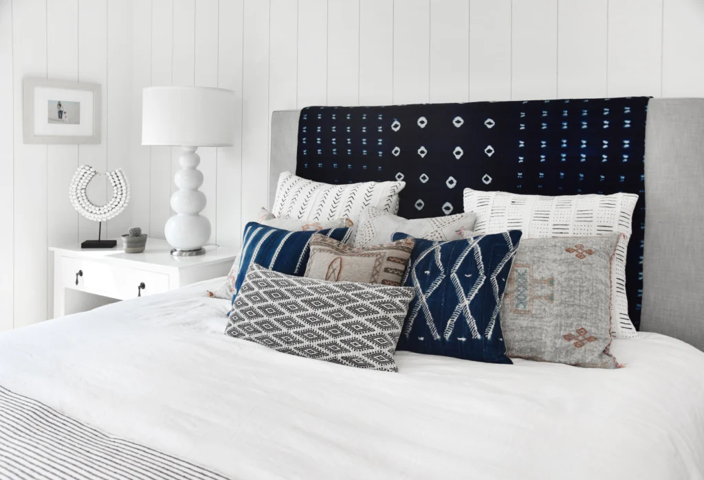 Whole-house remodel: Bed against white vertical shiplap wall with grey headboard and indigo patterned pillows