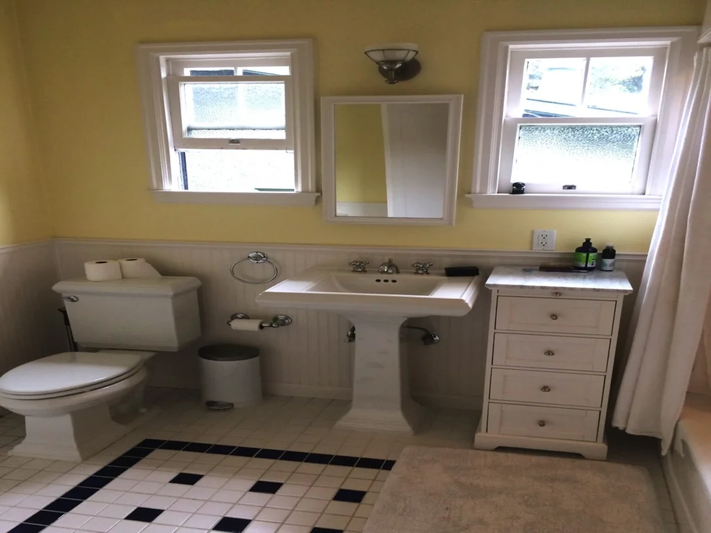 Bathroom remodel: Pedestal sink and toilet with white beadboard wainscot, yellow walls and black-and-white tile floor
